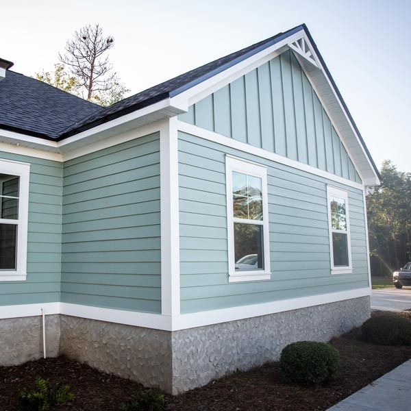 Light blue house exterior with white trim, gabled roof, and gray foundation along a landscaped walkway
