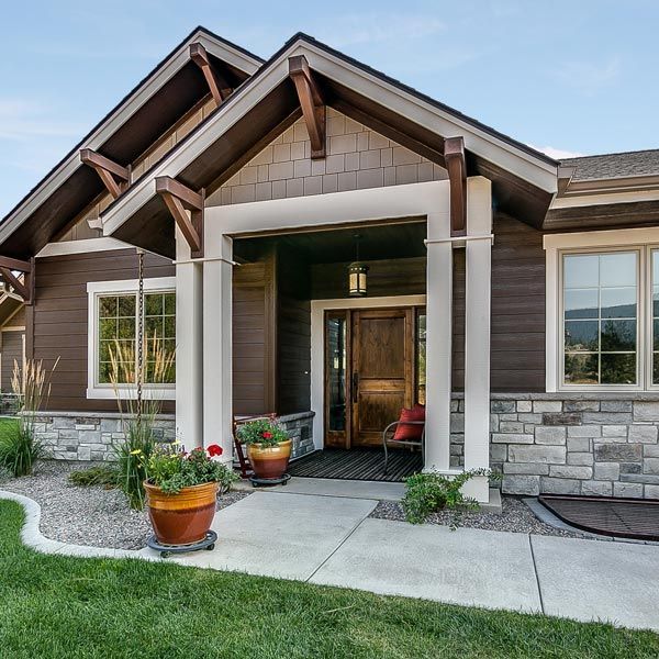 Modern house front entrance with stone and wood exterior, potted plants, and a concrete walkway