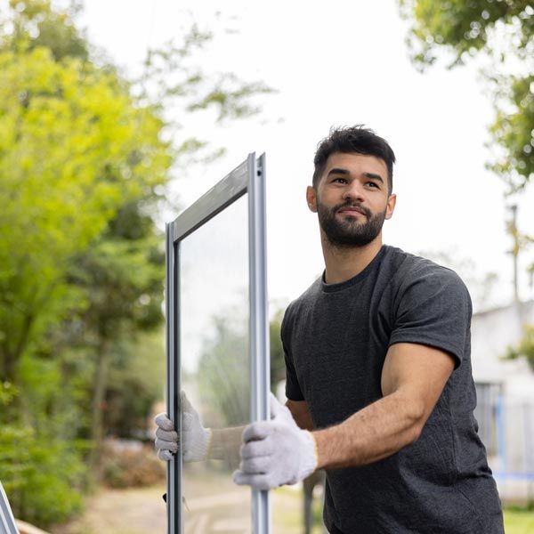 Man in gloves carrying a glass door panel outdoors near greenery