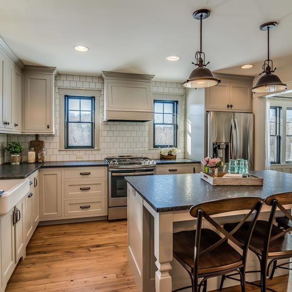Bright modern kitchen with white cabinets, wood floors, stainless appliances, and a dark island with stools