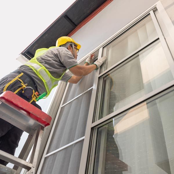 Worker in yellow hard hat cleaning a window on a building exterior with a squeegee