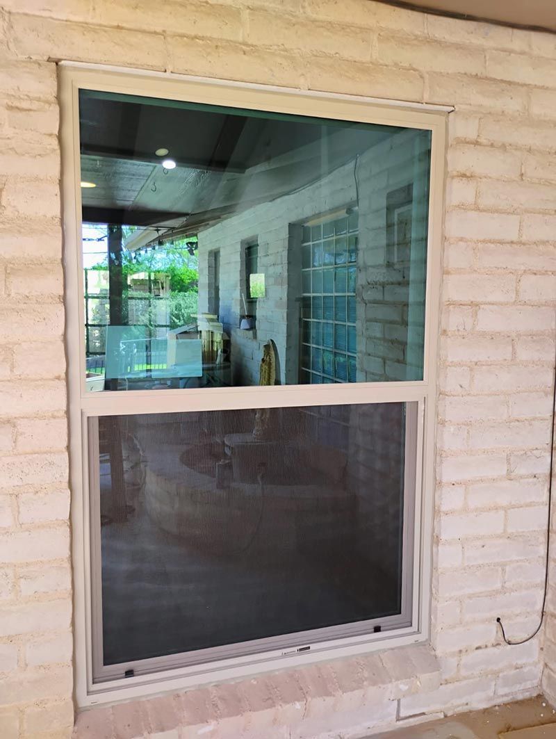 White-framed window in a brick wall, showing a dim interior and patio reflection.