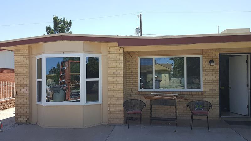 Single-story tan house exterior with bay window, front window, and two chairs on the patio