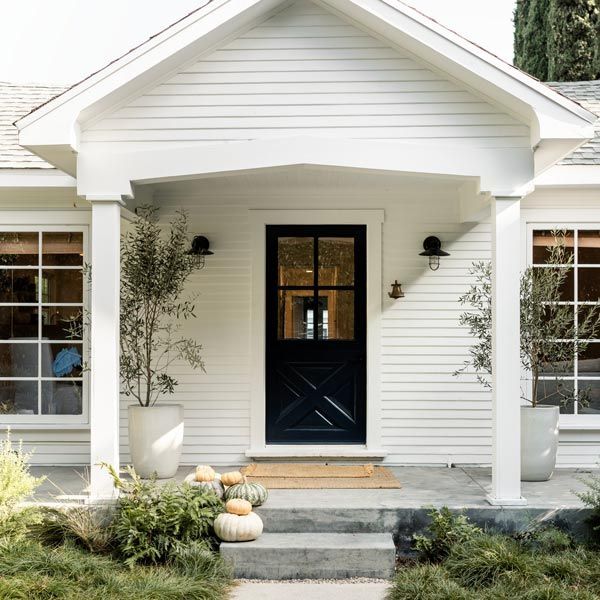 White house front porch with black door, columns, steps, and potted pumpkins in the entryway