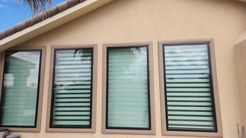 Four narrow windows with green blinds on a tan stucco building under a sloped roof.