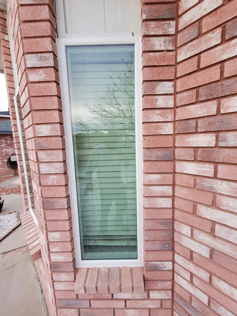 Tall narrow window with white trim set into a red brick wall, reflecting trees and sky.