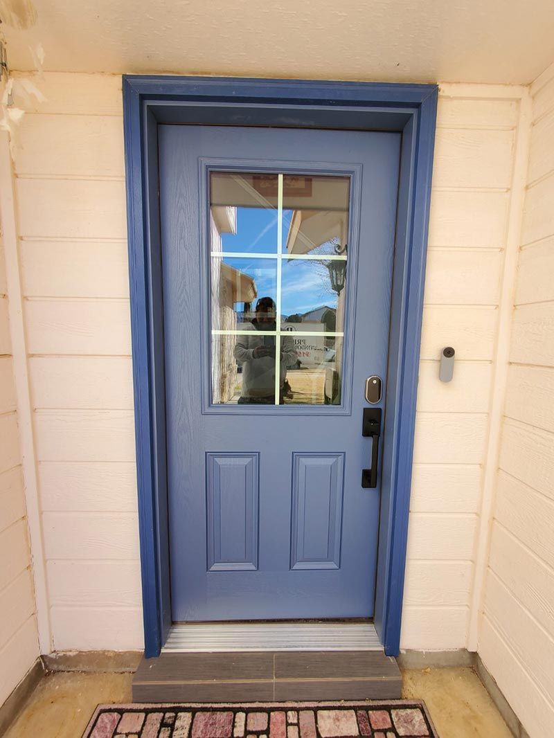 Blue front door with window panes and black handle, set in a light brick entryway.