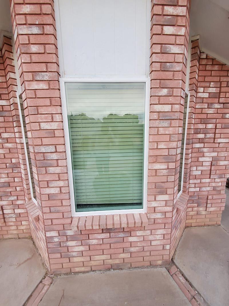 Brick exterior wall with a narrow white-framed window and closed blinds.