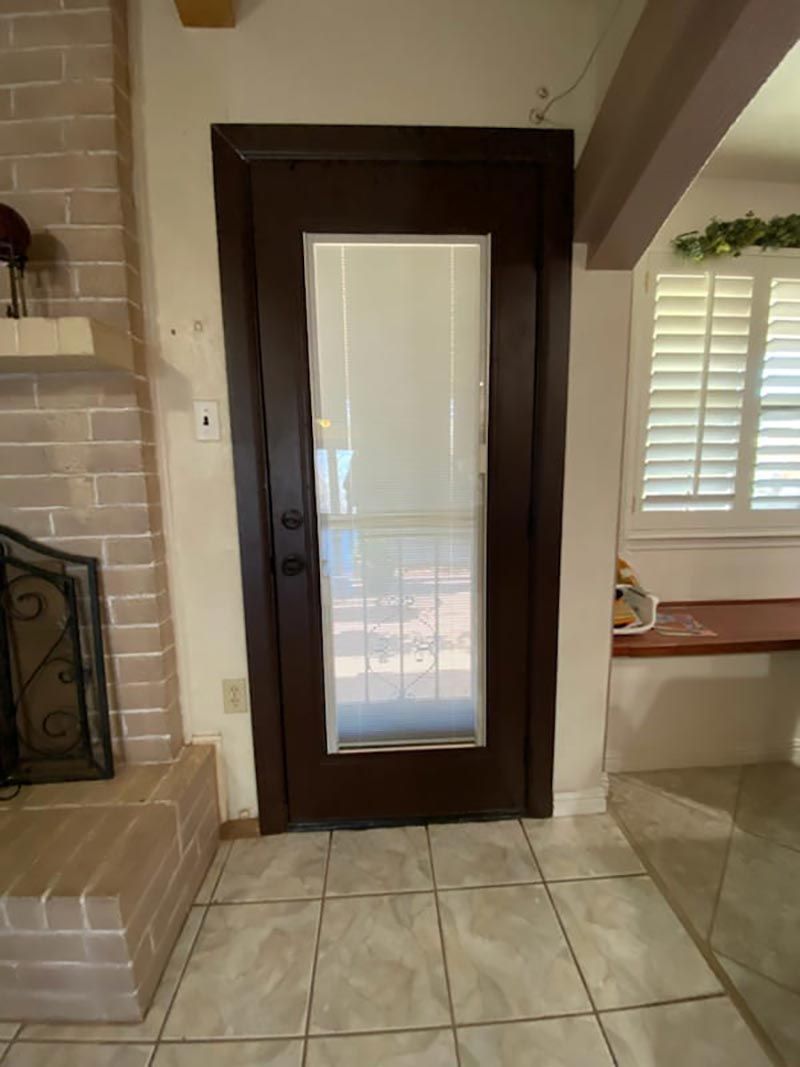 Glass-paneled front door beside a brick fireplace in a tiled entryway