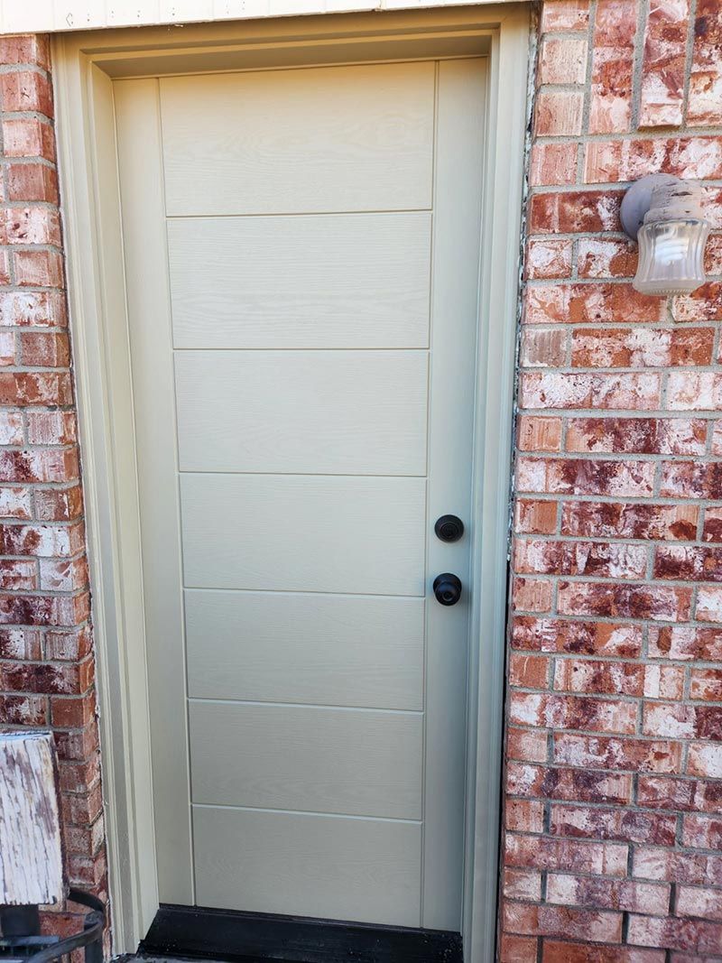 Closed beige front door in a red brick exterior wall with a black knob and deadbolt