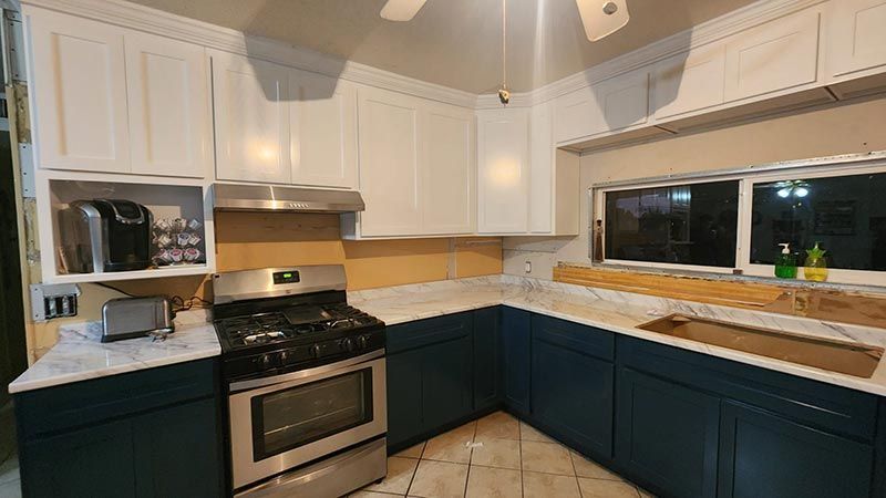 Bright kitchen with white cabinets, dark lower cabinets, stainless stove, and a large window over the sink.