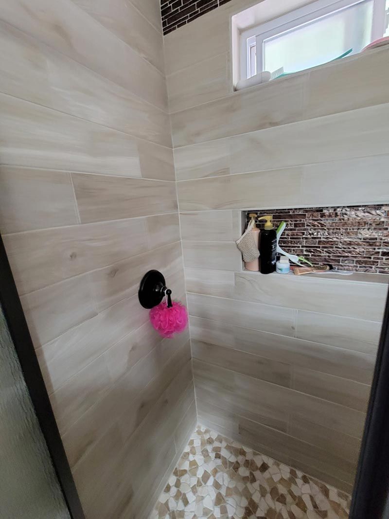 Small tiled shower stall with a wall niche, black shower fixture, and pink loofah.