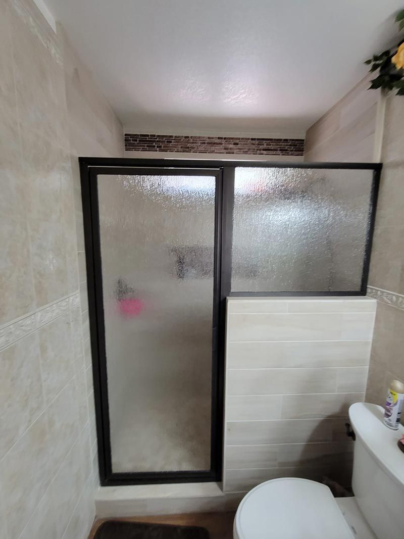 Small bathroom with frosted glass shower doors, a white toilet, and a tiled half-wall beside the sink.