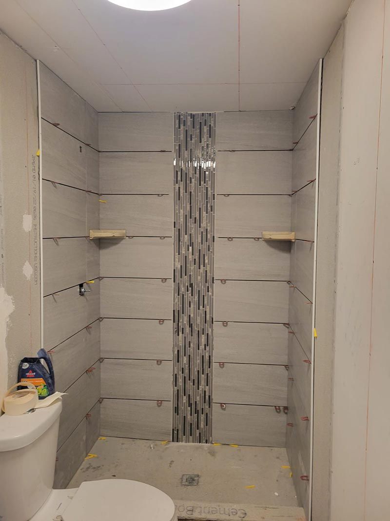 Small bathroom with tiled shower stall, built-in shelves, and a toilet in the foreground.