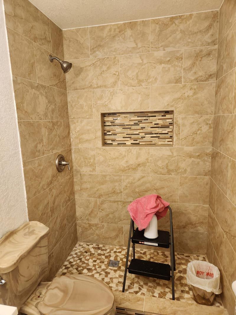 Small beige tiled shower room with a shower chair, pink cloth, and cleaning bucket.