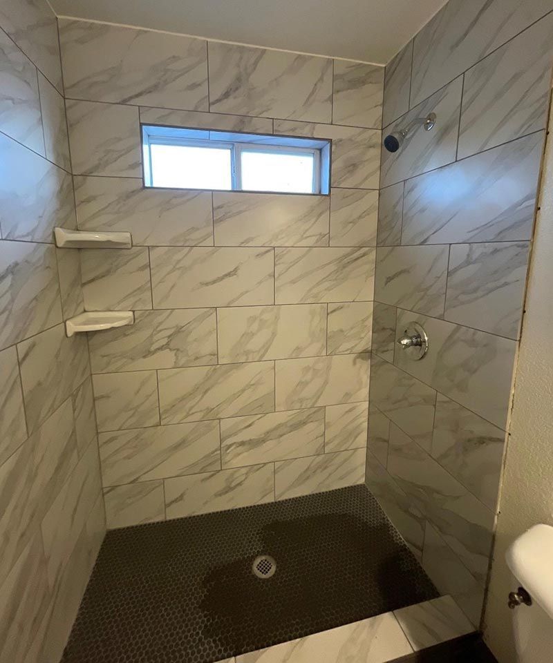 Accessible tiled walk-in shower with grab bars, shelves, small window, and black shower floor.