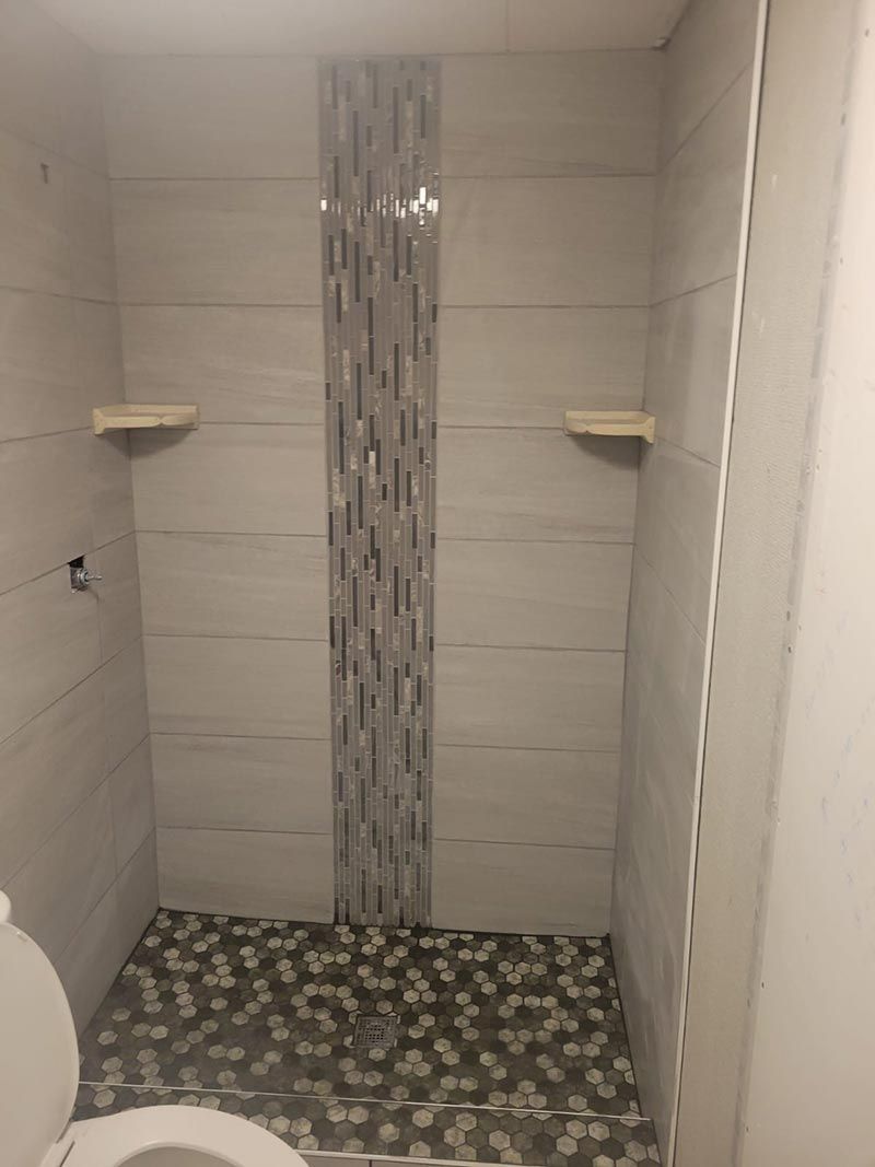Small tiled shower with a mosaic floor and two corner shelves.