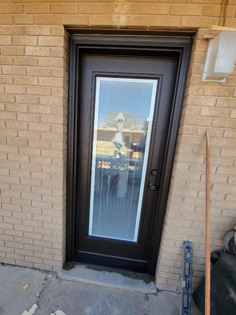 Black-framed glass door in a tan brick wall, with a reflection in the window.