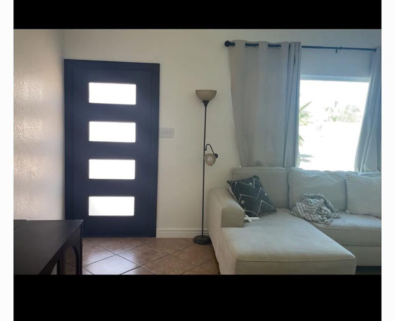 Small living room with white sofa, floor lamp, dark door, and bright window with curtains.