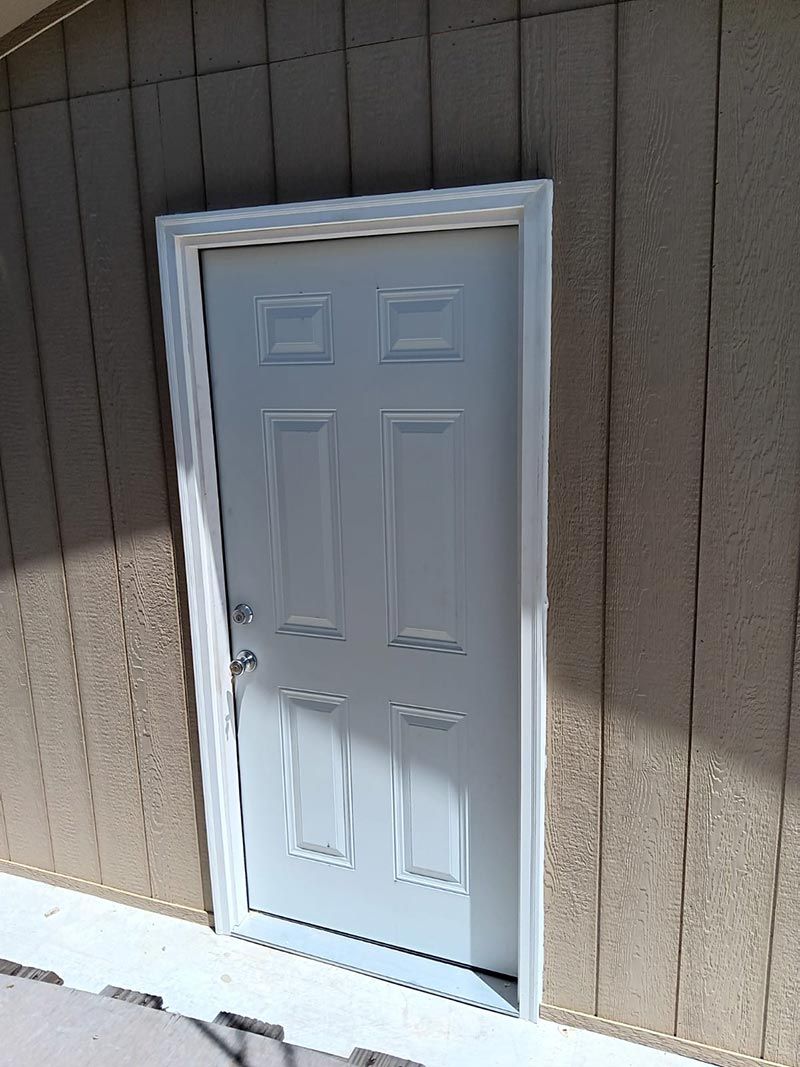 White exterior door with brass knob in a brown paneled wall, partially lit by sunlight.