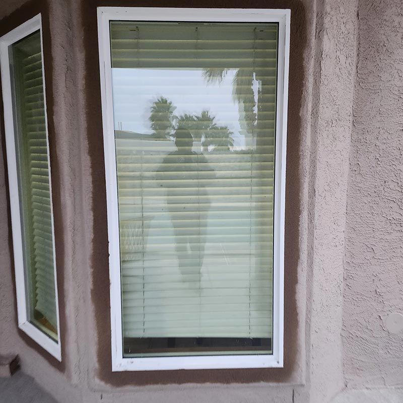 Window with white blinds reflecting a person’s silhouette on a beige stucco wall