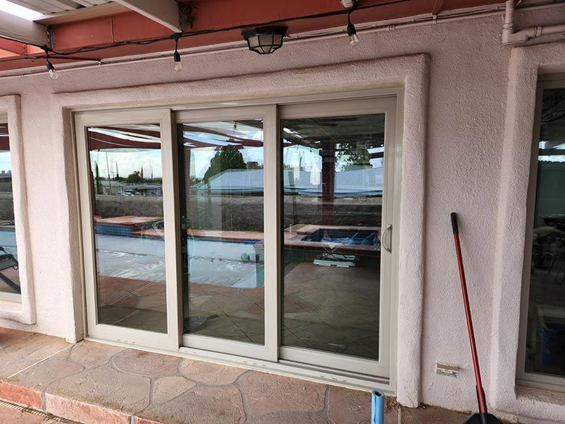 White sliding glass patio doors on a pink stucco wall with a broom leaning nearby