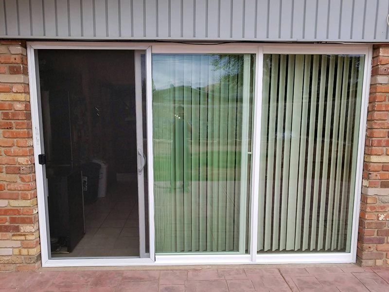 Sliding glass patio door with vertical blinds on a brick house exterior