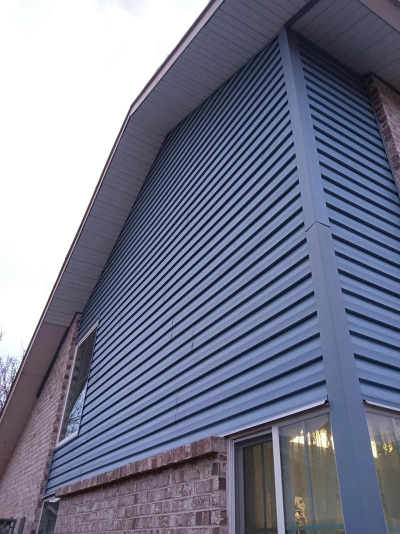 Blue-sided building with vertical siding and a brick lower wall, viewed from below.