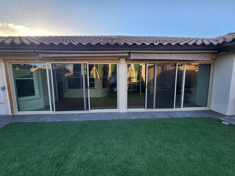 Backyard patio with large sliding glass doors and a tiled roof over a green lawn.