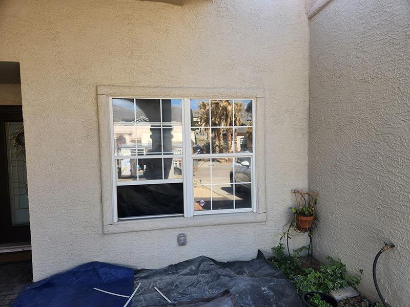 Small stucco patio wall with a white-framed window and potted plant beside a covered object.