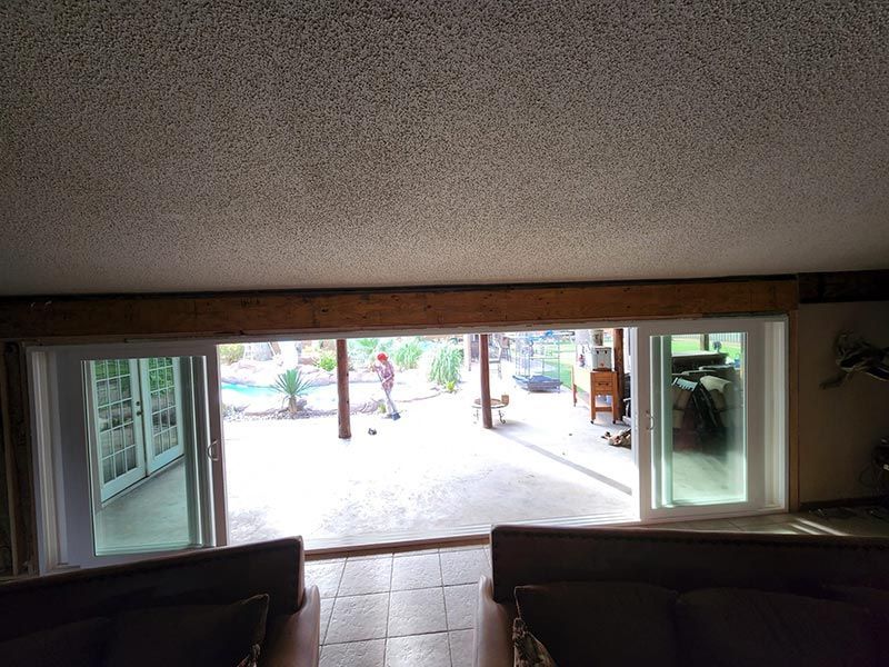 Indoor view through open doors to a bright outdoor patio with trees and a sidewalk.