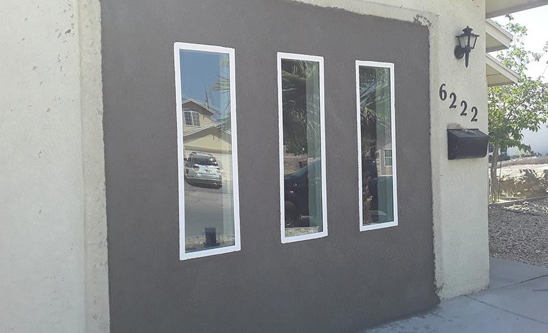 Gray stucco house facade with three narrow windows, black mailbox, and house number 6222 by the door