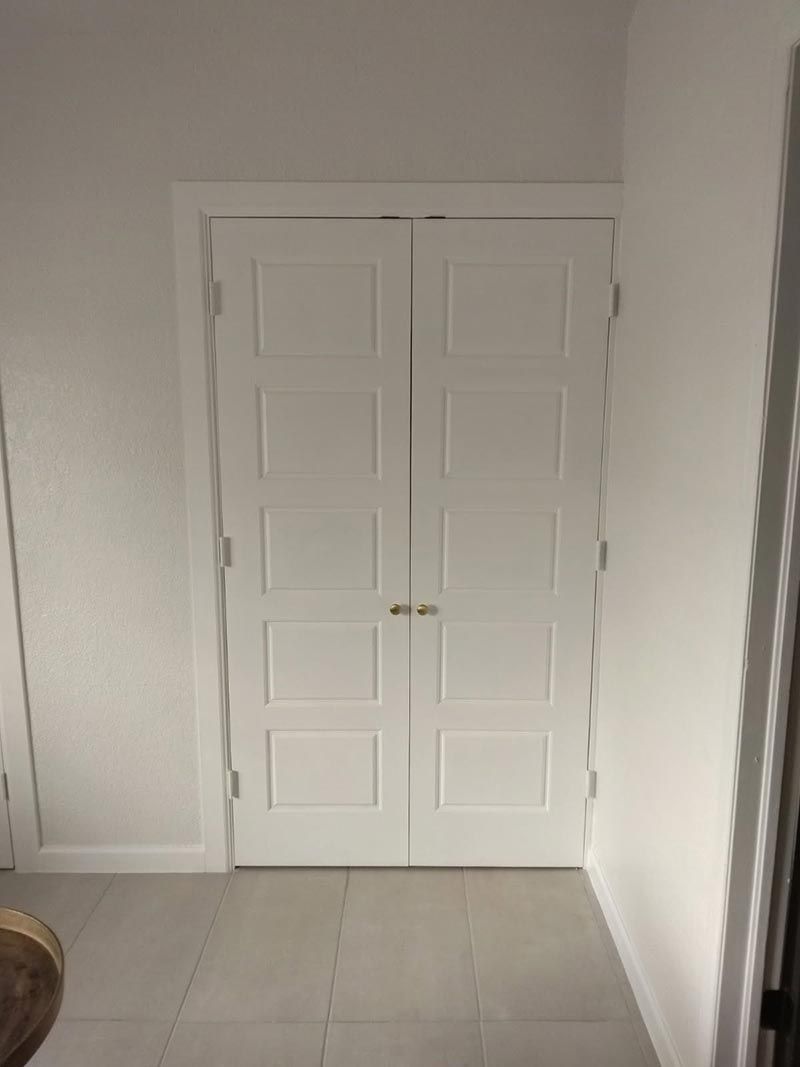 White double closet doors in a plain room with light-colored tile flooring.