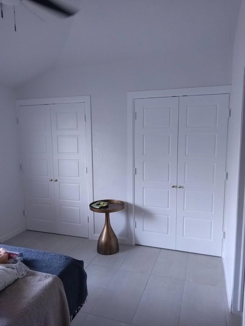 White bedroom with two closed closet doors and a small round side table near the wall.