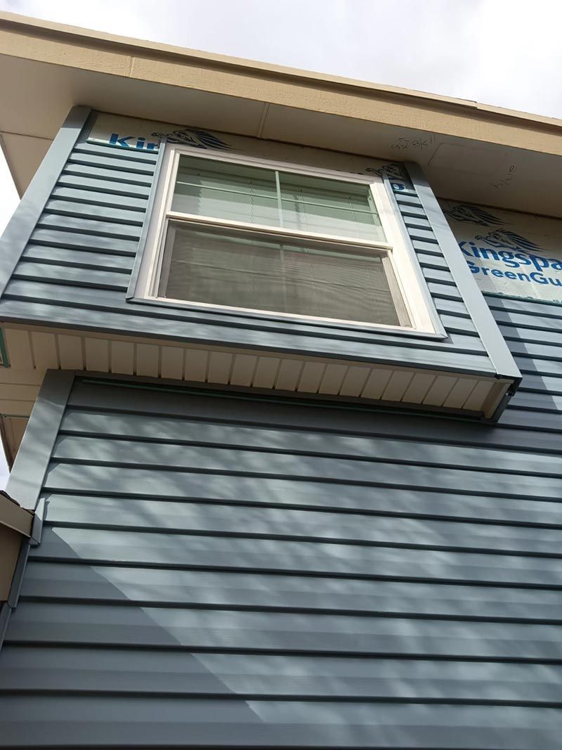 Blue house siding with a white-trimmed window under a roof overhang