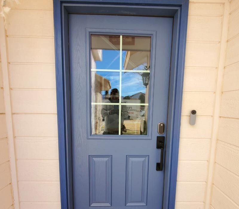 Blue front door with a window and black handle on a light-colored house exterior