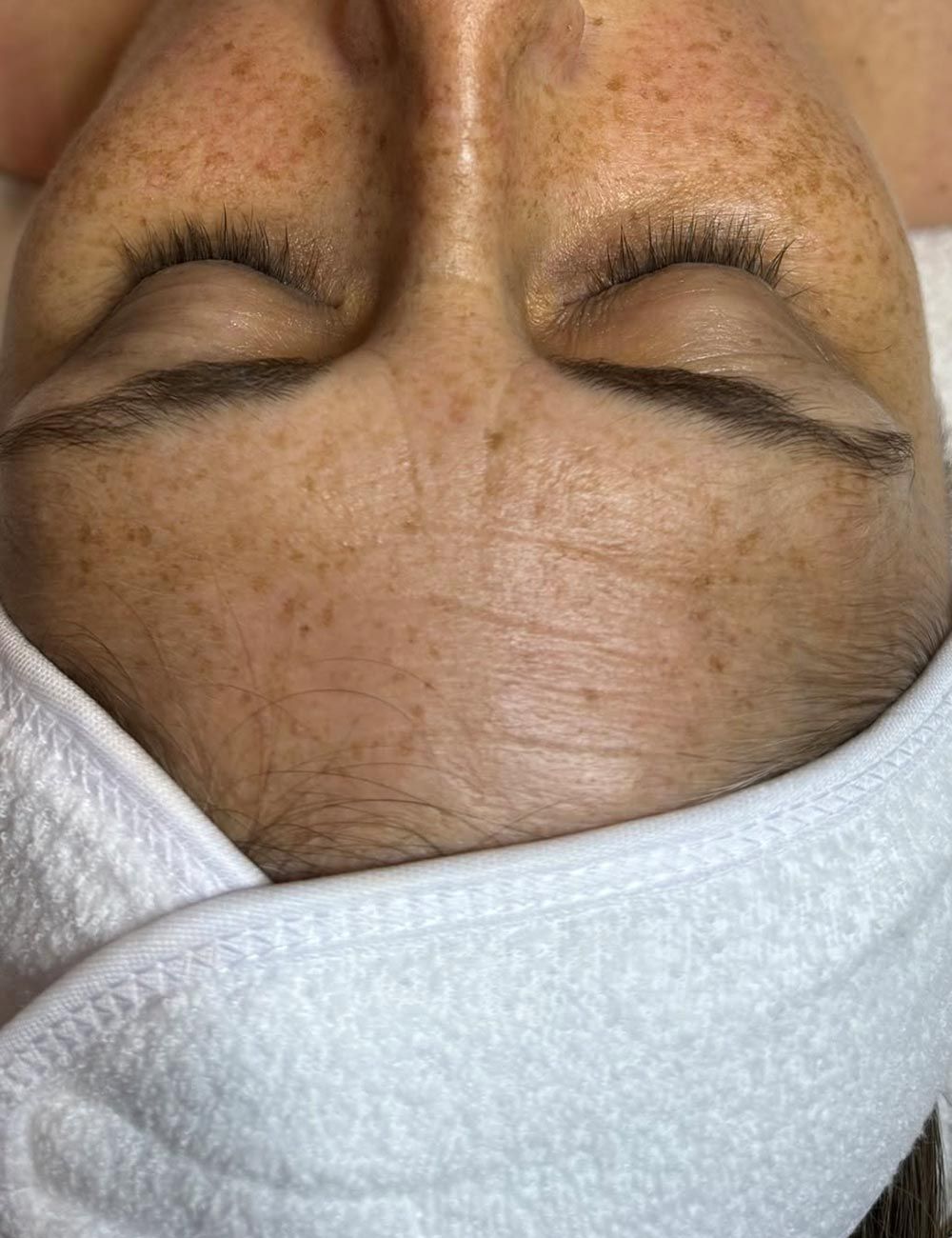 Close-up of a person’s face with eyes closed, wrapped in a white towel or headband.