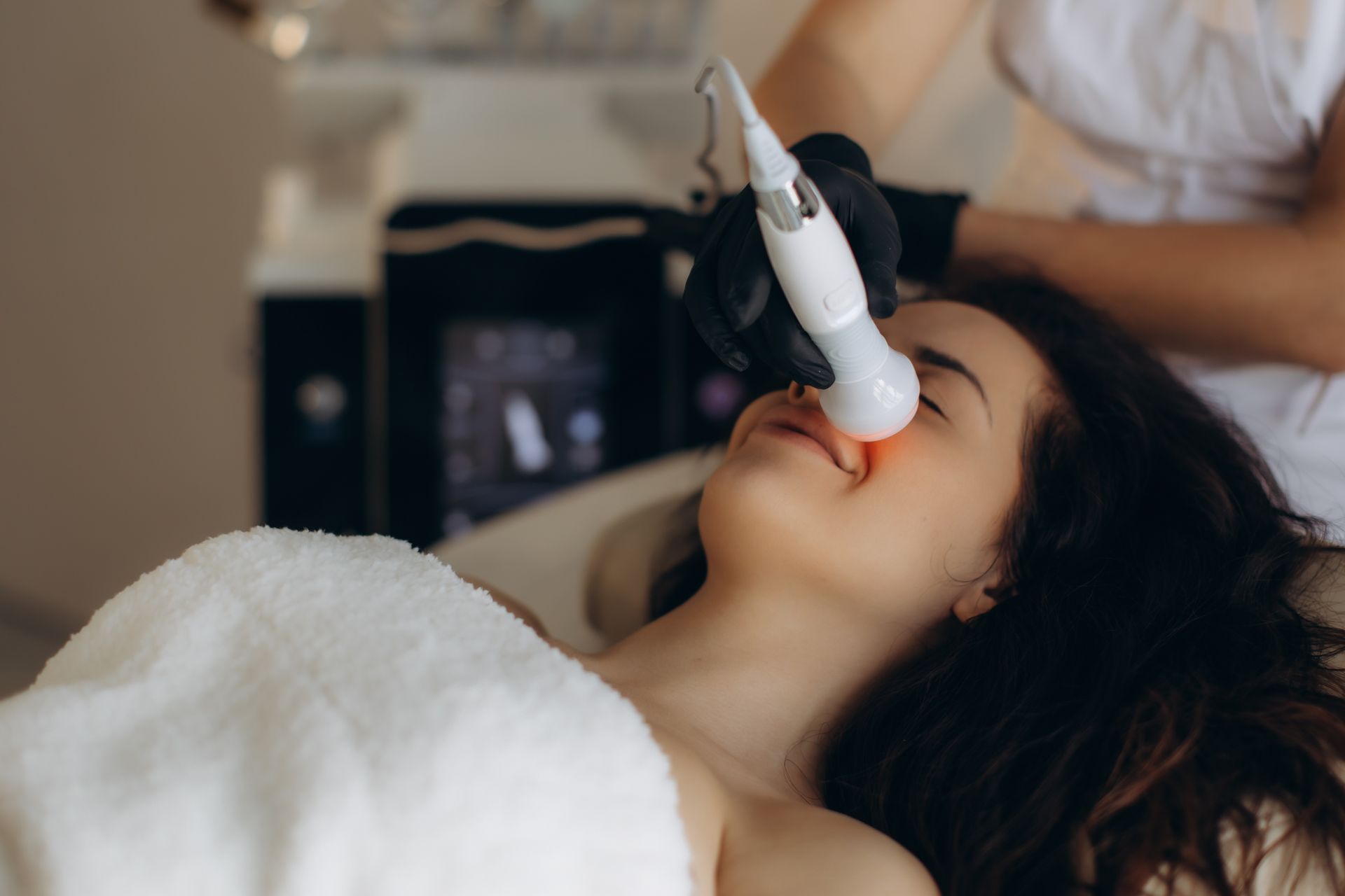 Person receiving a facial treatment with a device while lying on a treatment bed