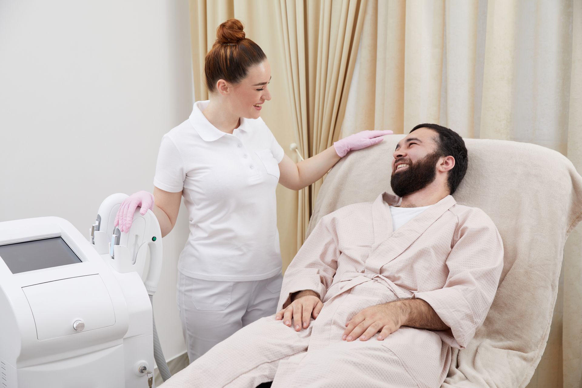A clinician checks a reclining patient beside a medical laser device in a treatment room