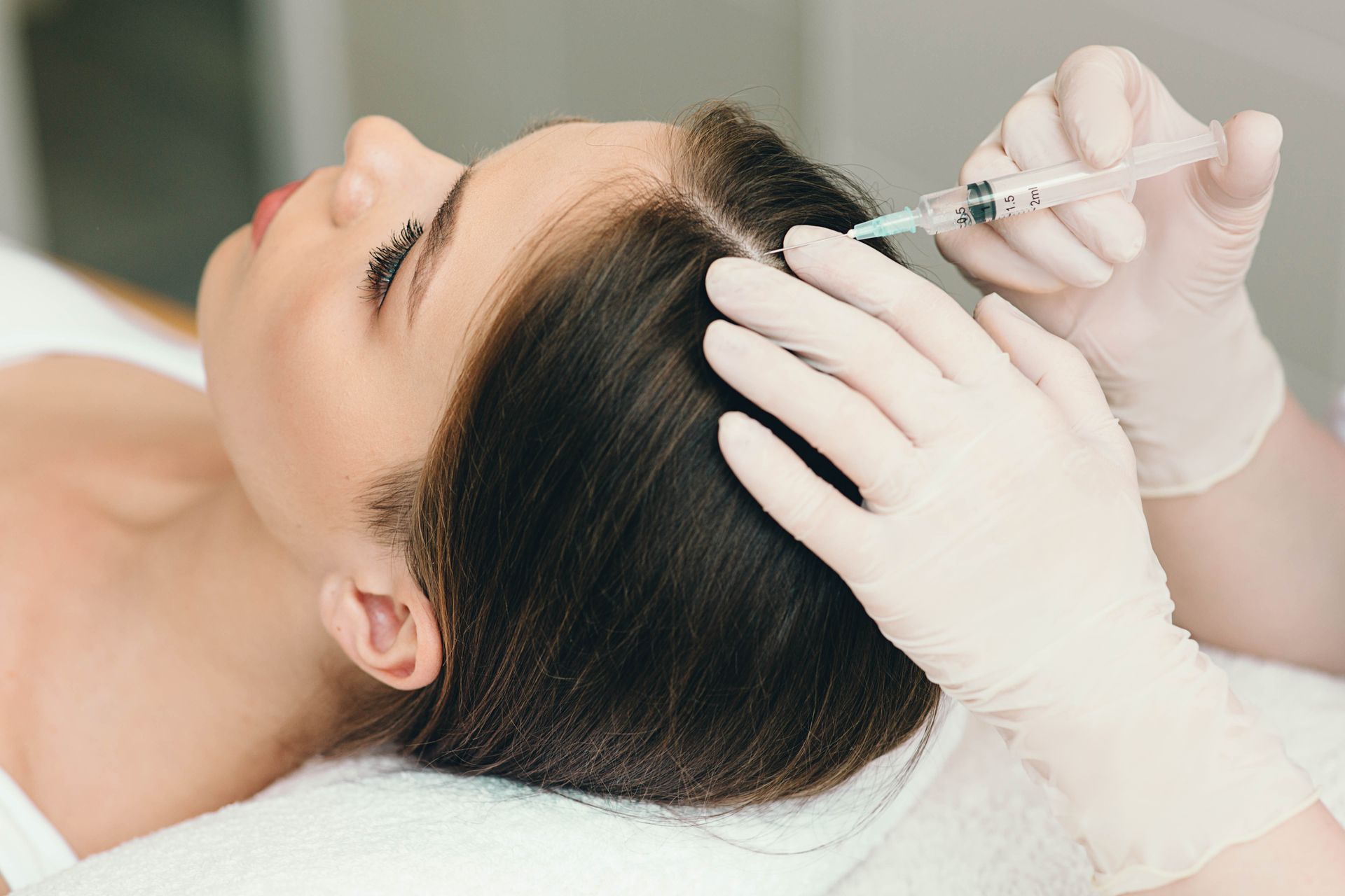 Gloved hands inject a woman’s scalp with a syringe during a cosmetic treatment