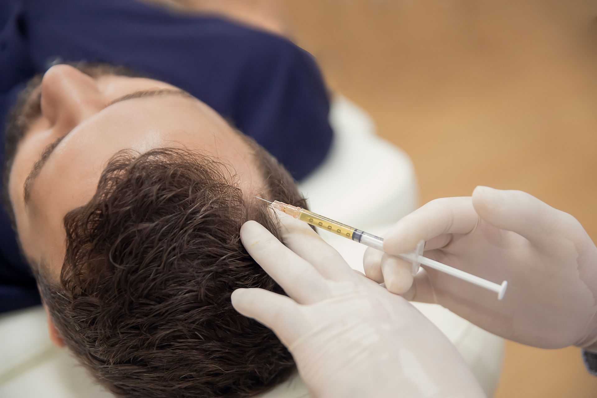 Gloved hands inject a man's temple with a syringe during a cosmetic treatment
