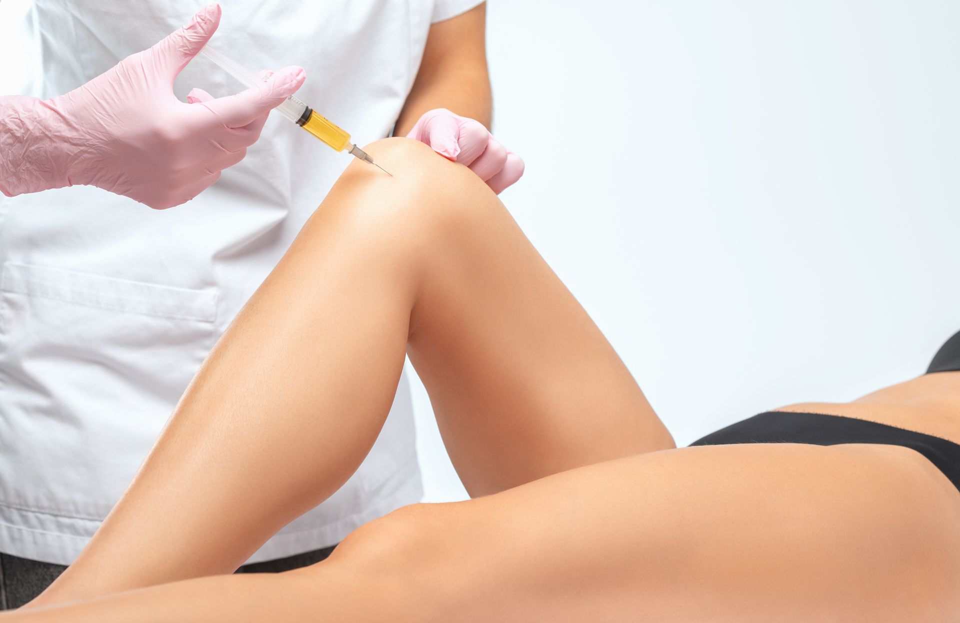 Gloved clinician injecting a patient’s bent knee in a clinical setting