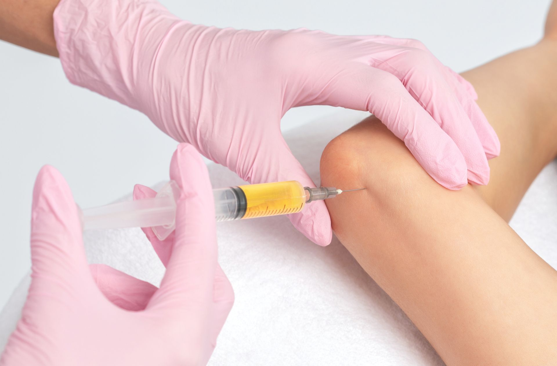 Gloved hands administering a syringe injection into an arm with a yellow-tinted liquid