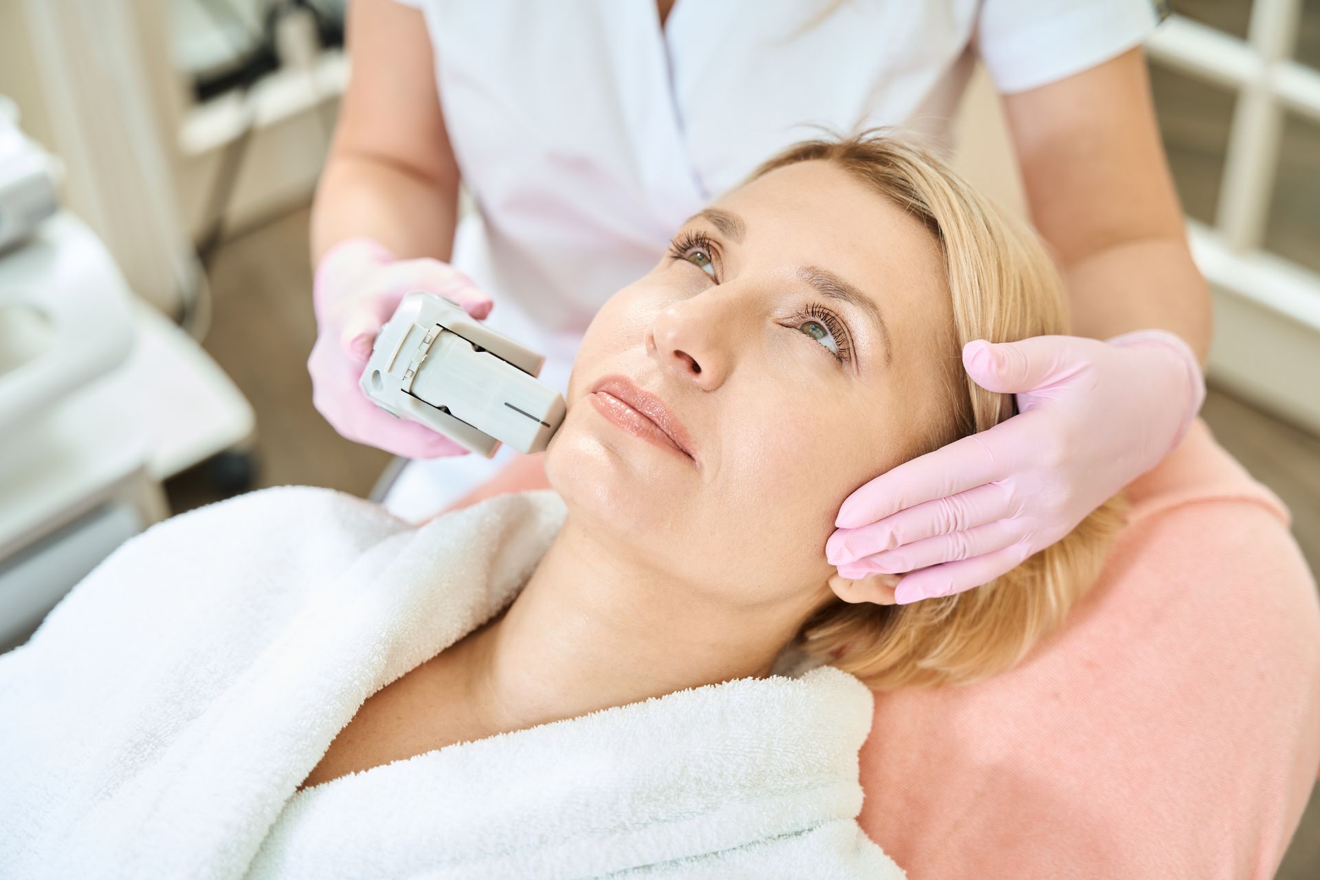 Cosmetic treatment on a reclining client with a facial device and gloved hands in a spa setting