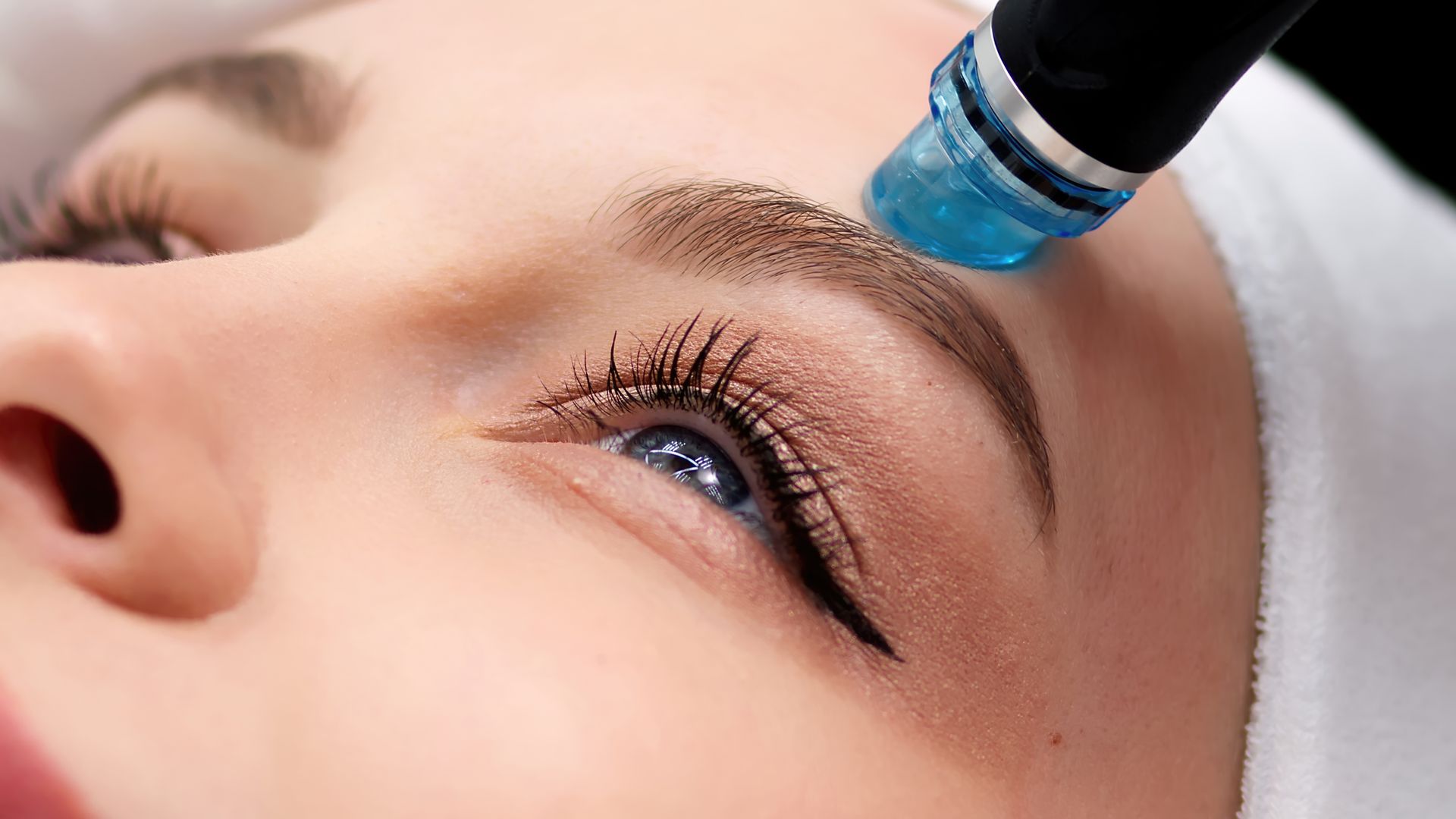 Blue cosmetic applicator near a woman's eye during an eyebrow treatment Blue cosmetic applicator near a woman's eye during an eyebrow treatment