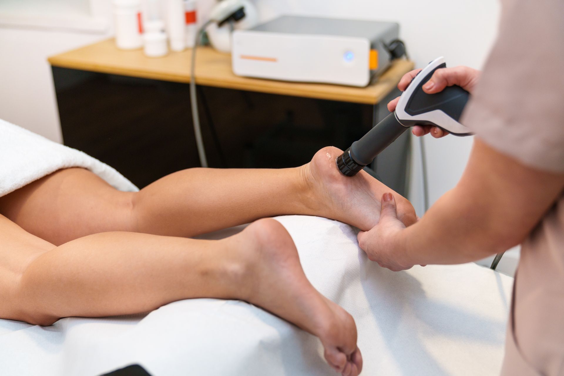 Podiatrist treating a patient’s foot with a handheld medical device in a clinic exam room