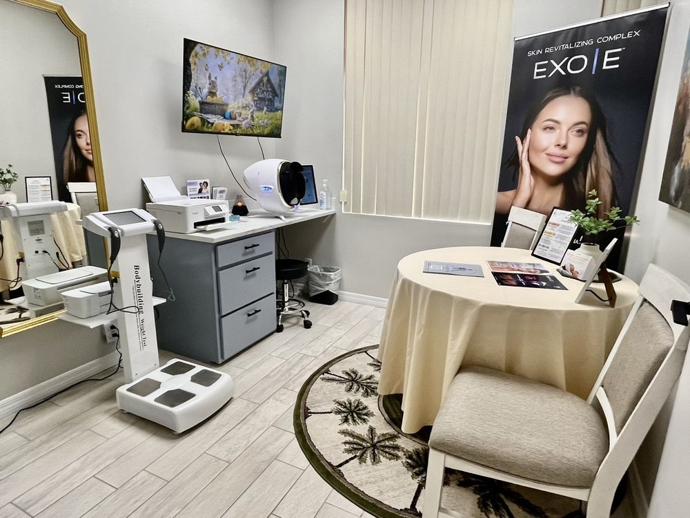 Medical spa treatment room with facial machines, white chairs, and a round table beside an EXO|E poster.