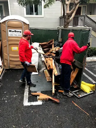 Two men are working on a pile of wood in a parking lot.