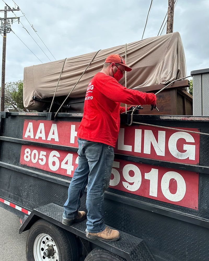 A man in a red shirt is standing on the back of a dumpster.