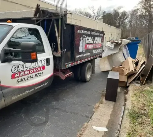 A white C&L Junk Removal truck parked near a curb, with debris piled nearby.